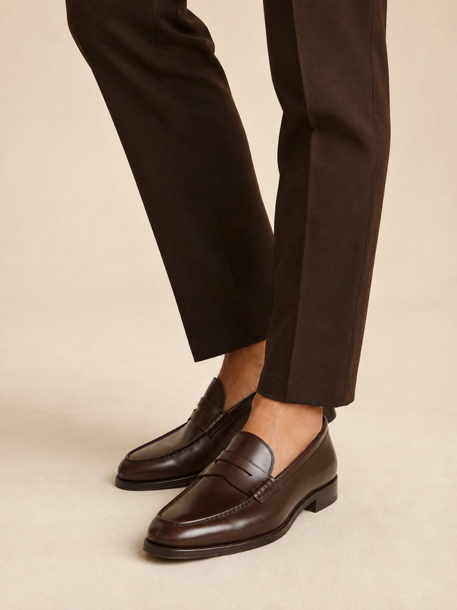 Polished dark brown penny loafers worn with chocolate tailored trousers