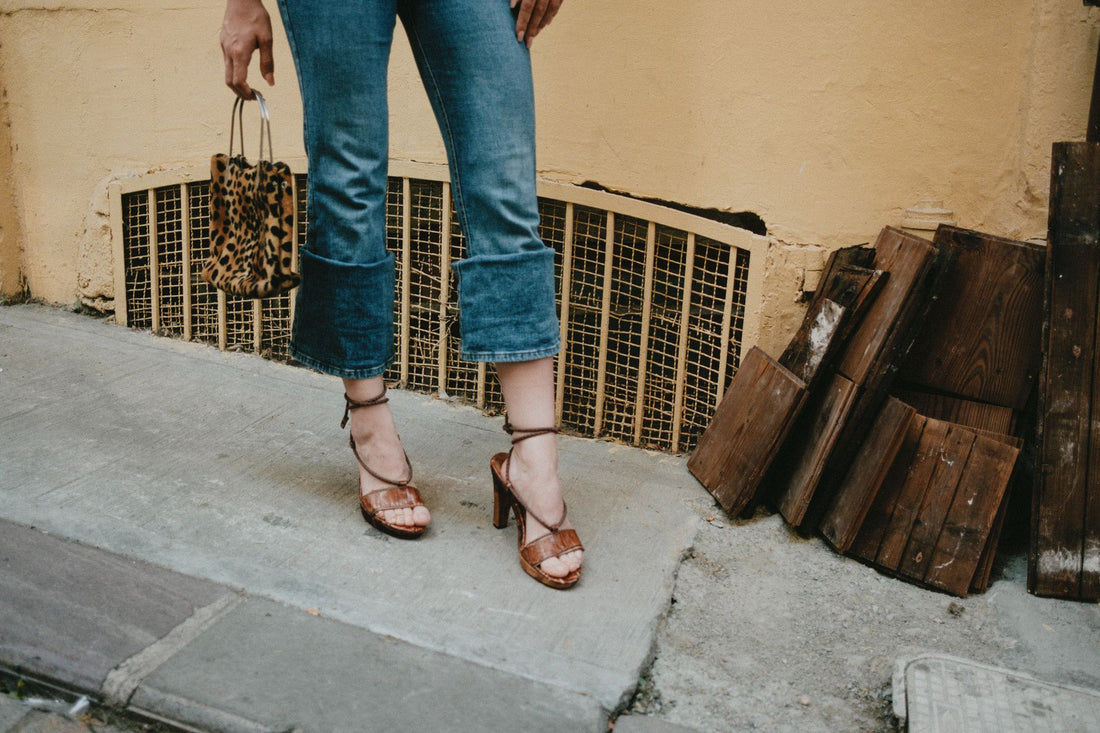 Leopard print bag carried with cropped denim and tan heeled sandals against an ochre wall