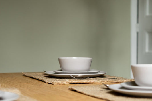 Simple white stoneware stacked on a woven mat on a warm wooden dining table