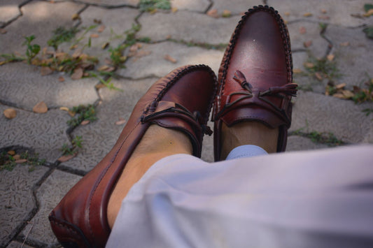 Burgundy tassel loafers worn with cream trousers on a sunlit stone path