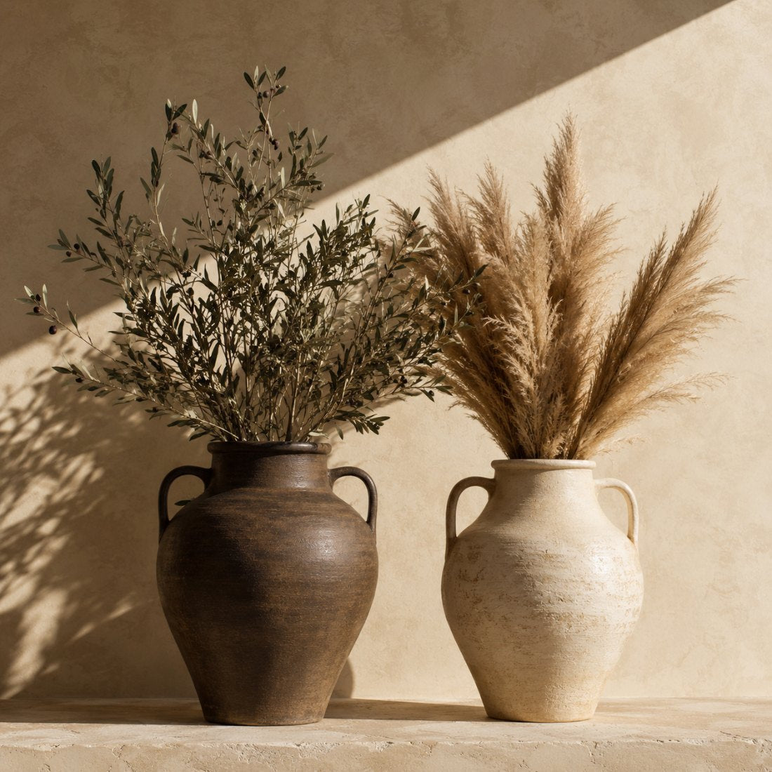 Bronze and cream ceramic vases with olive branches and pampas on a sunlit plaster ledge